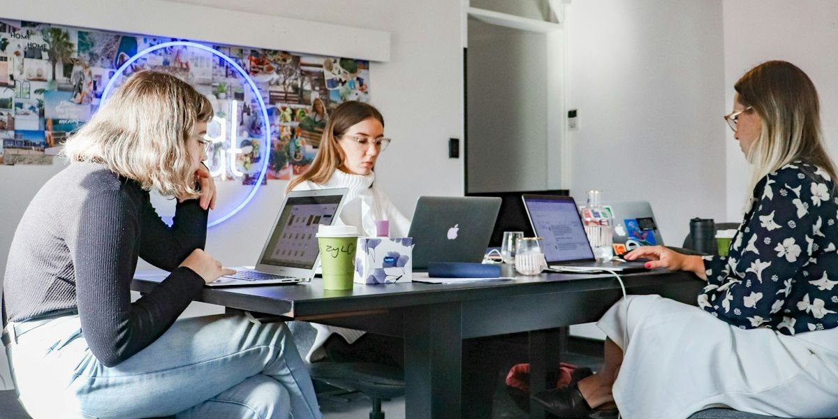 3 women sitting on chair in front of table with laptop computers